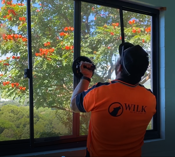 Man in high vis shirt replacing window looking out towards tree with orange flowers